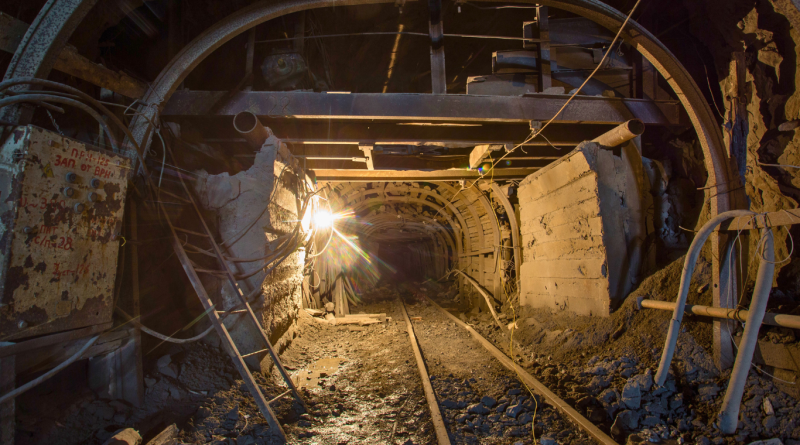 Underground subsurface mining tunnel with metal beams and railway tracks.