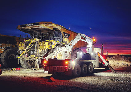 a Caterpillar 797F ultra-class mining haul truck alongside a specialized support vehicle operated by Thompson Construction Group