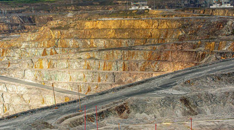 Large-scale open-pit copper mine with terraced excavation benches and exposed rock.